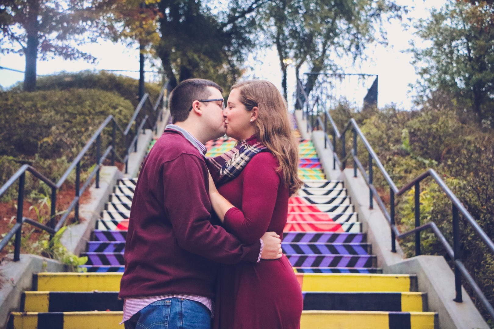 Haleigh and Sean kissing in front of a flight of stairs that have been painted with artistic patterns
