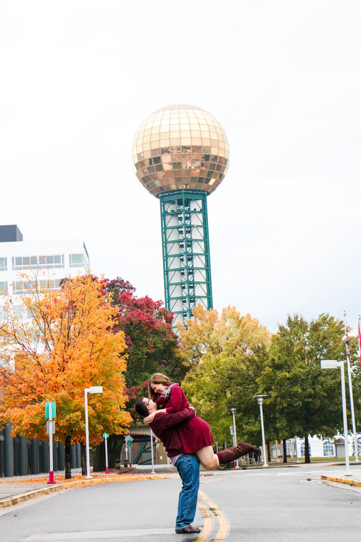 Sean picking up and holding Haleigh in the middle of the road at World's Fair Park with the Sunsphere visible in the background
